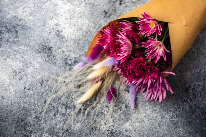 Bouquet of aster flowers wrapped in paper on stone background with copy space