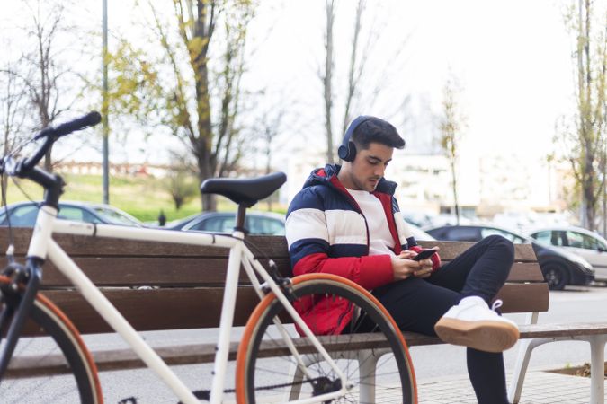 Man with bicycle checking smartphone while sitting on bench