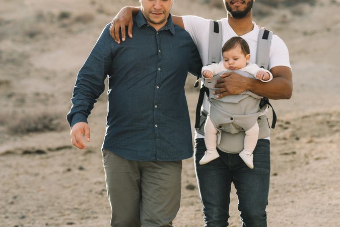 Unrecognizable diverse men walking with baby on nature