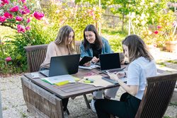 Three university college students studying in the garden at home preparing for exams, taking notes.