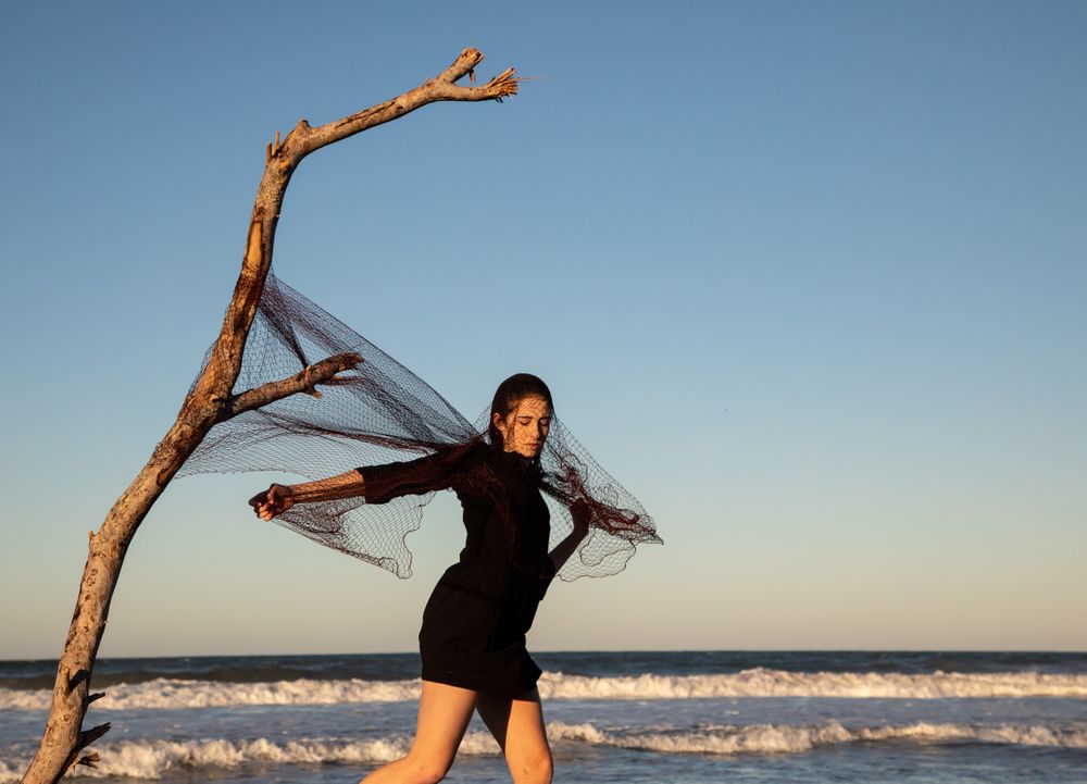 Woman in fishing net fixed on twig near water on shore