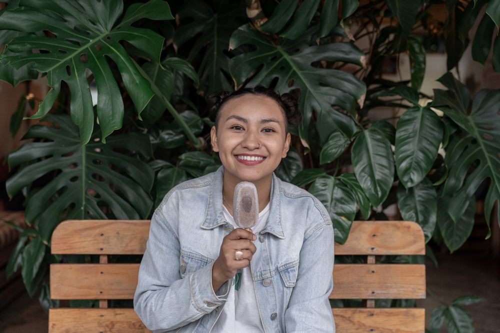 A young Hispanic woman is smiling while eating an ice cream