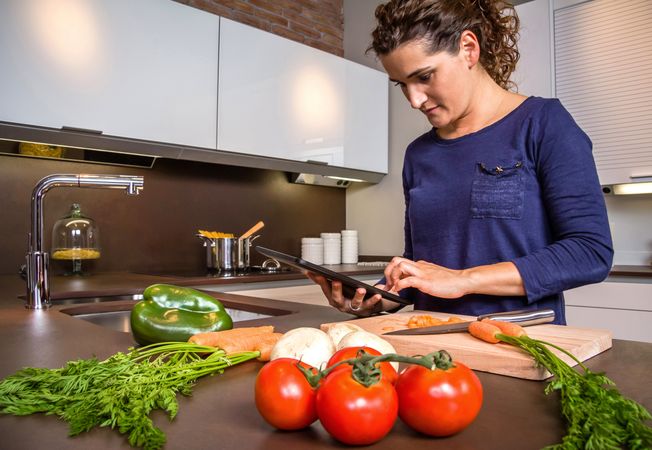 Woman checking digital tablet for recipe as she prepares dinner
