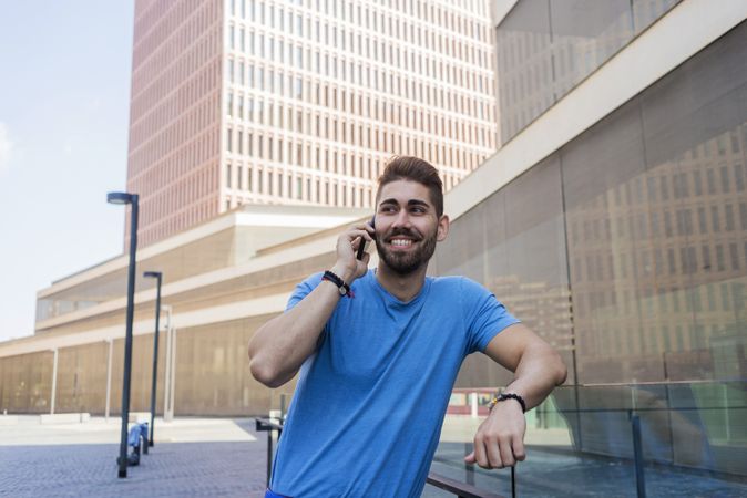 Happy man leaning on glass railing outside having conversation on mobile phone