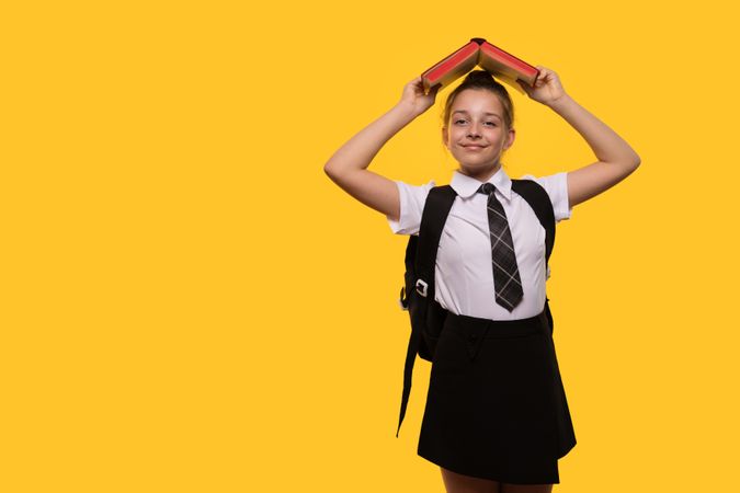 Schoolgirl wearing uniform holds book over her head.