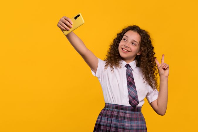 Smiling girl taking selfie, making peace sign.