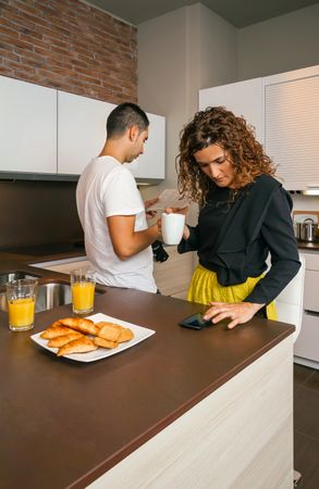 Couple checking phone and newspaper while having breakfast at home before work