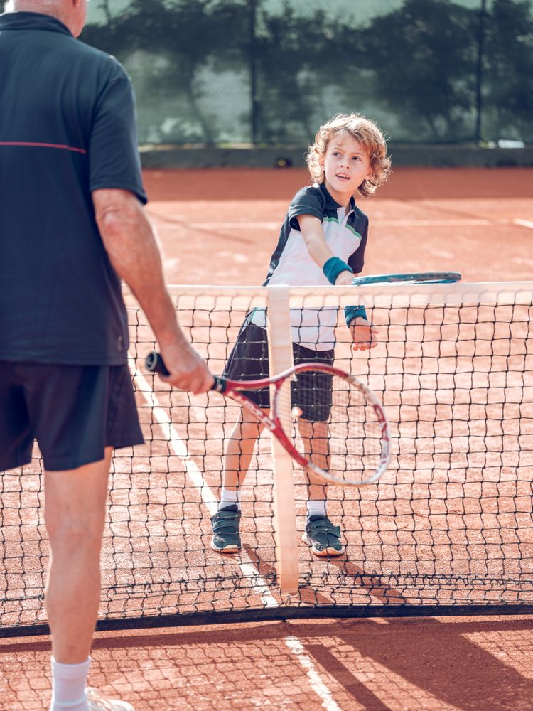 Active little boy practicing tennis with crop male instructor