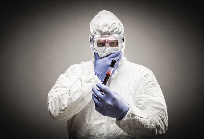 Man Wearing HAZMAT Protective Clothing Holding Test Tube Filled With Blood