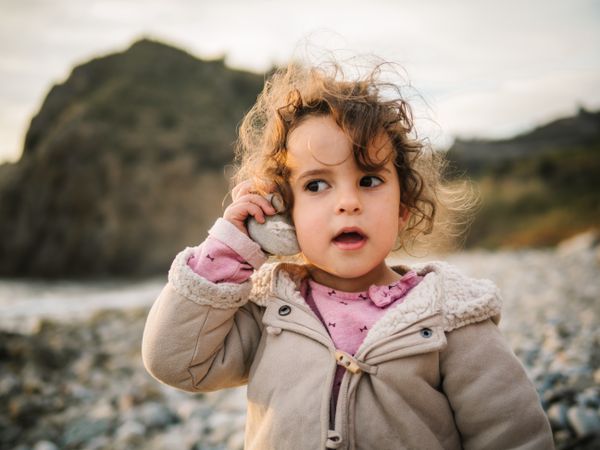 Toddler girl playing with seashell on beach