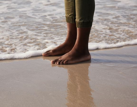 Cropped image of Black person's feet standing on seashore