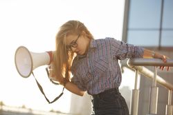 Woman hanging off railing with megaphone dressed in checkered shirt