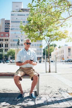 Mature man sitting on a city bench with a mobile phone