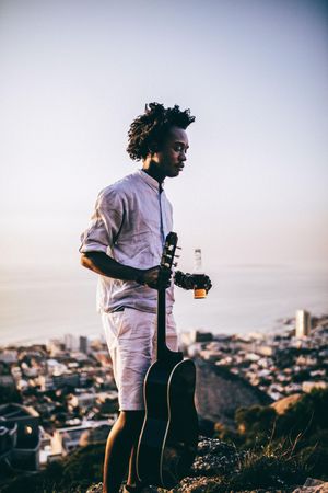 Young man holding a guitar and beer outdoors