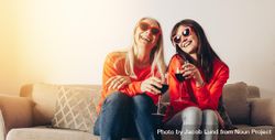 Older mother and adult daughter wearing sunglasses toasting with wine inside at home 4mDDe5