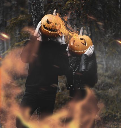 Two people in dark outfits wearing jack o lantern hat standing in the woods