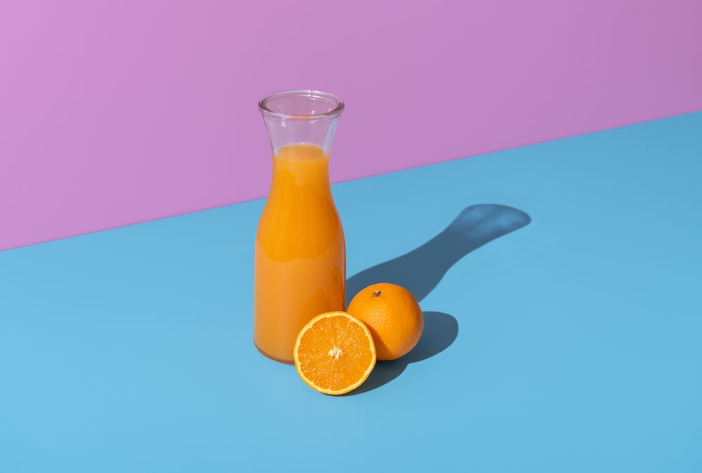 Orange juice carafe and orange fruits isolated on a vibrant background