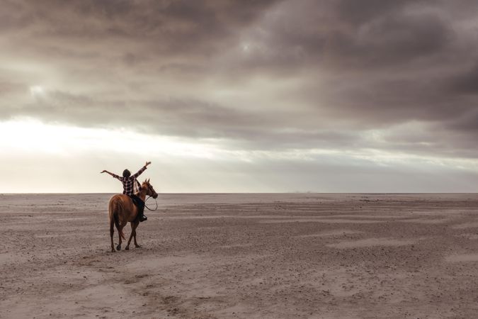 Woman riding a horse on beach with her hands wide spread