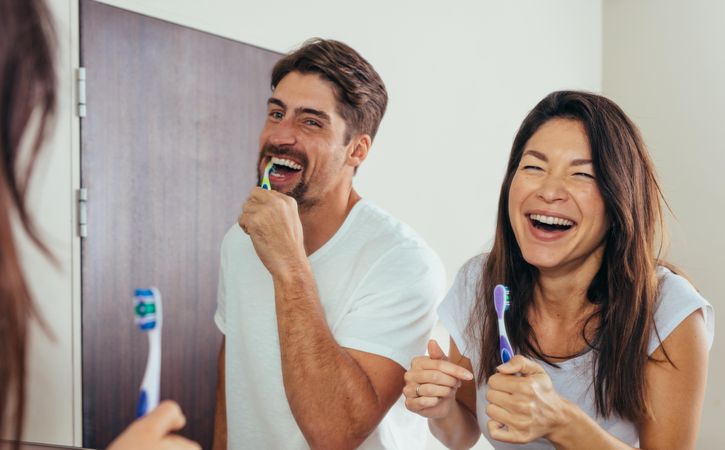 Smiling man and woman brushing teeth in bathroom