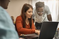 Young woman and Black man collaborating at laptop in modern workspace with warm light and focused teamwork