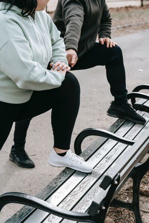 Jogging man and woman stretching legs on wooden bench