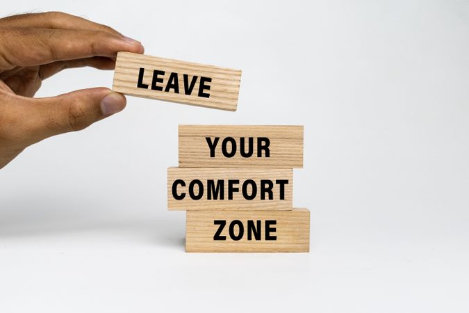 male hand put leave your comfort zone words on wooden blocks isolated on plain background