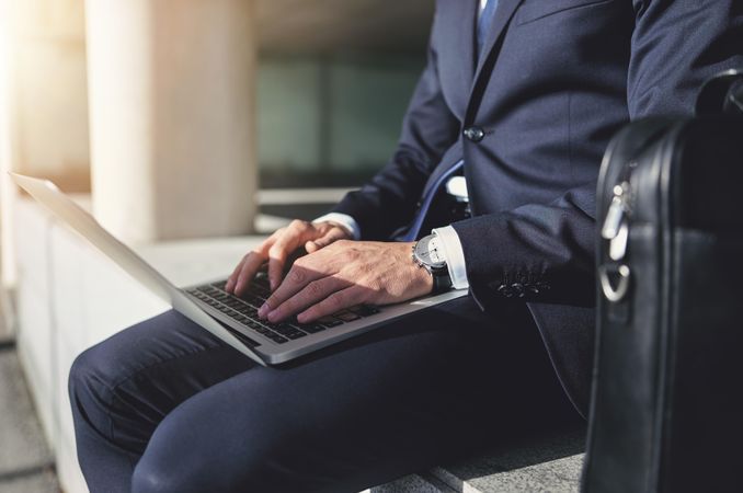 Cropped shot of man in business attire working on his laptop outside