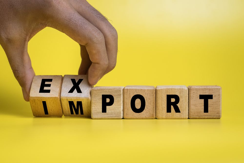 male hand turning export and import words on wooden block isolated on yellow background