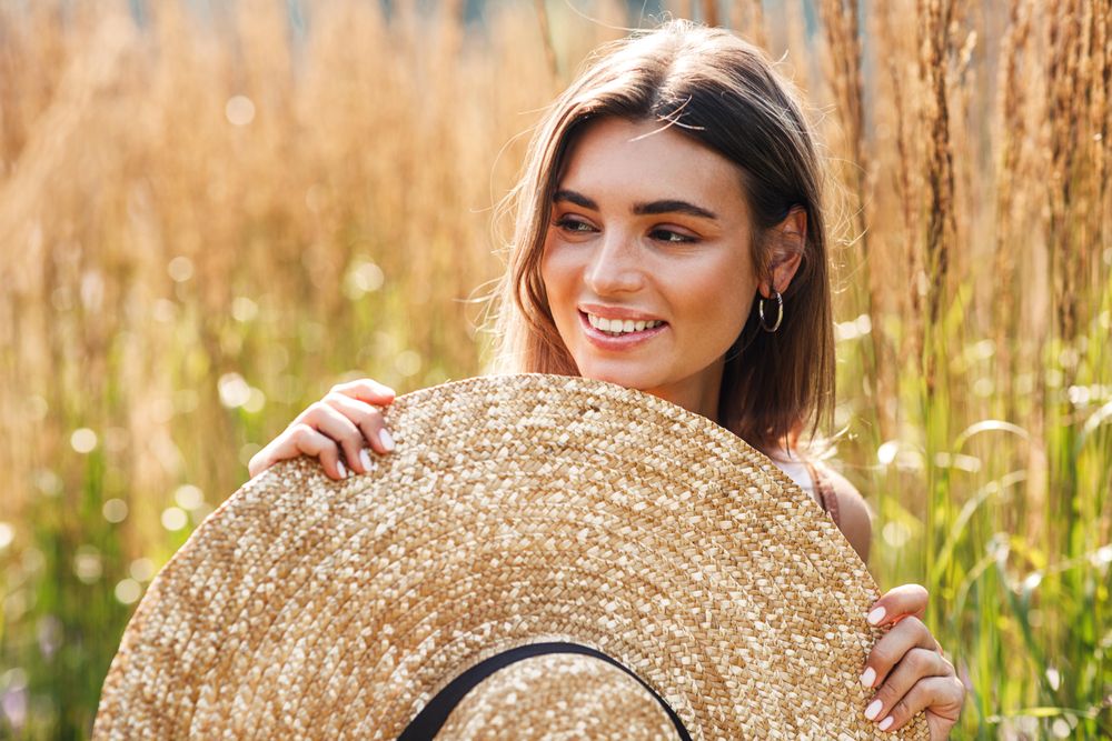 Woman standing in field outside holding up sunhat