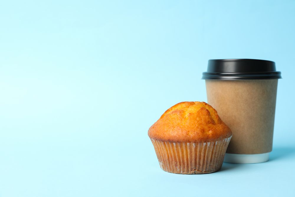Paper cup and chocolate muffin on blue background, space for text