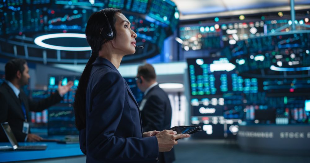 Female Investment Banker Wearing Headphones and Using a Tablet Computer with Financial Market Analytics Data.