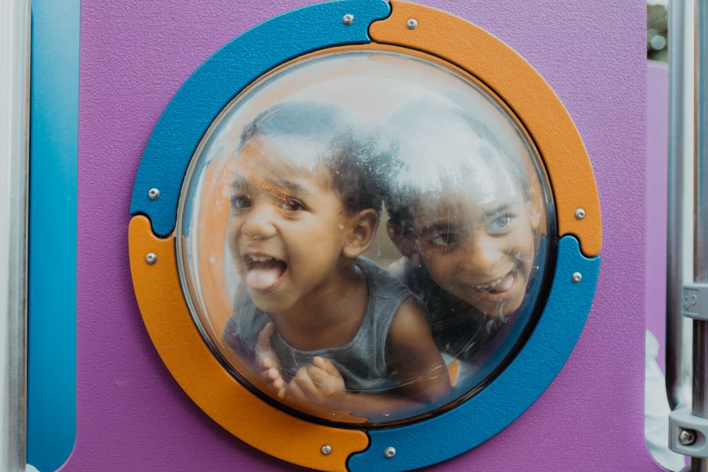 Funny Black boys behind porthole on playground
