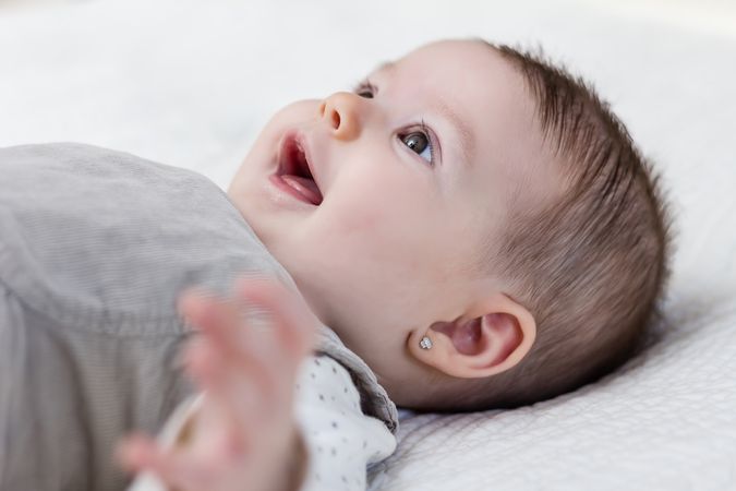 Happy baby girl lying on back over white bedcover.