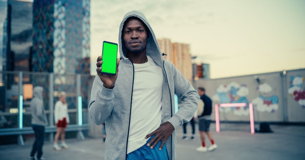 Black Man Holding a Smartphone, Showing the Green Screen Mock Up Display.