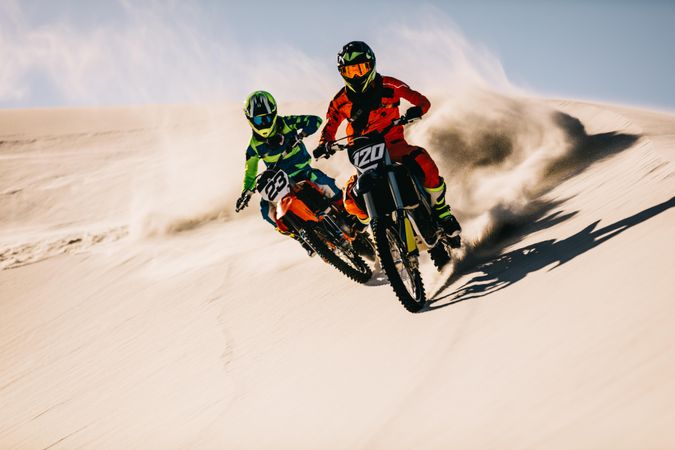Two dirt bikers riding on sand dunes