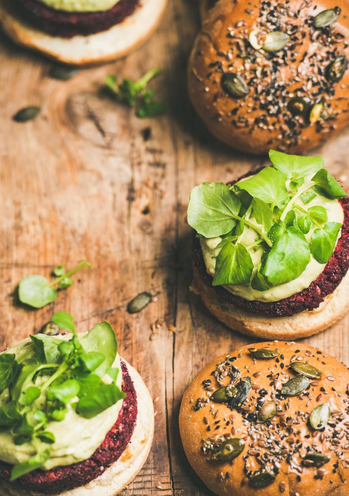 Close up, vegan burgers on seeded buns arranged on wooden board, vertical composition, copy space