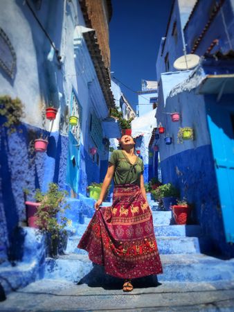 Laughing woman in long skirt standing in a blue alley in Chefchaouen, Morocco