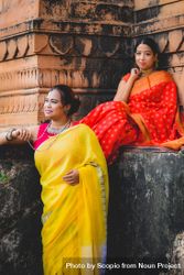 Two Indian woman in saris beside a carved wall bGQqx5