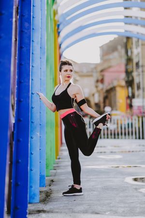 Woman with earphones stretching legs on street