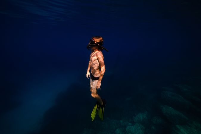 Teen boy in flippers swimming undersea in daylight