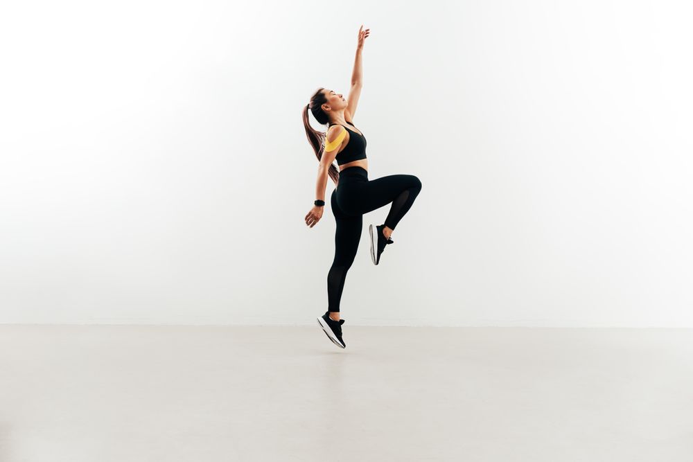 Woman jumping in the air against wall raising one hand up