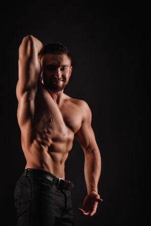 Bodybuilder competitor practicing arm and abs poses in dark studio