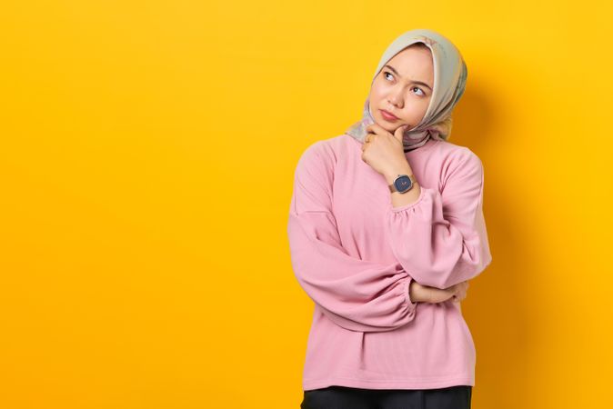 Muslim woman in headscarf in deep thought with head tilted and hand on chin