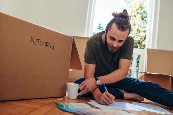 Man sitting with packing boxes around him and making a checklist