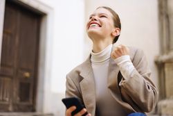 A Joyful Young Woman is Celebrating with a Smartphone While Enjoying the Outdoors