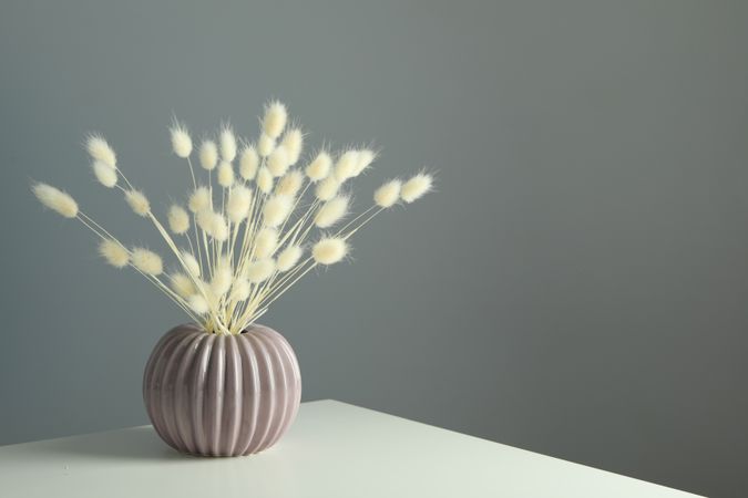Round and ridged vase in grey room filled with dried flowers with copy space