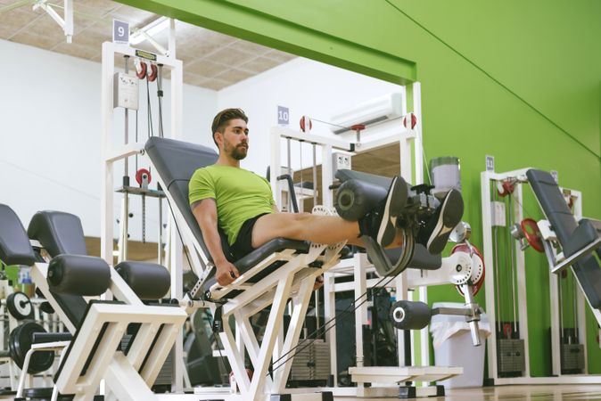 Male in green t-shirt working out quads using gym equipment