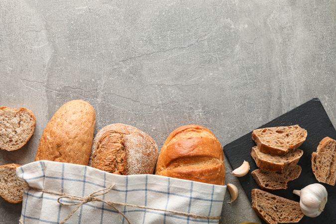 Composition with bakery products, garlic, olive oil and kitchen towel on grey background, top view and space for text