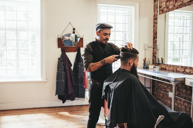 Hipster barber trimming customer’s hair