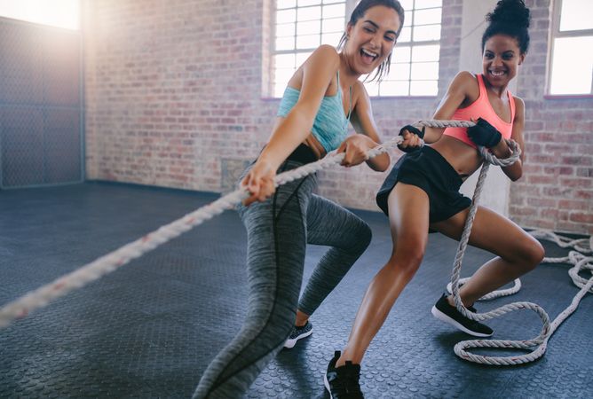 Shot of two young women smiling while exercising with rope at a gym